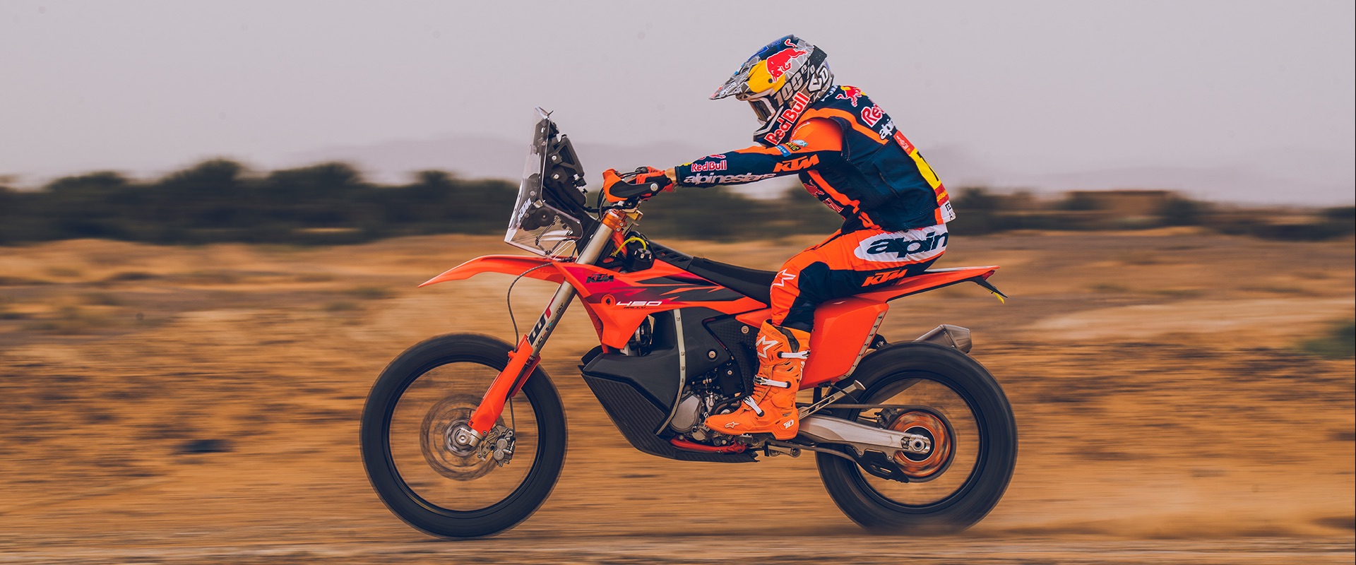 A KTM rally rider flat out across a flat, dusty desert plain