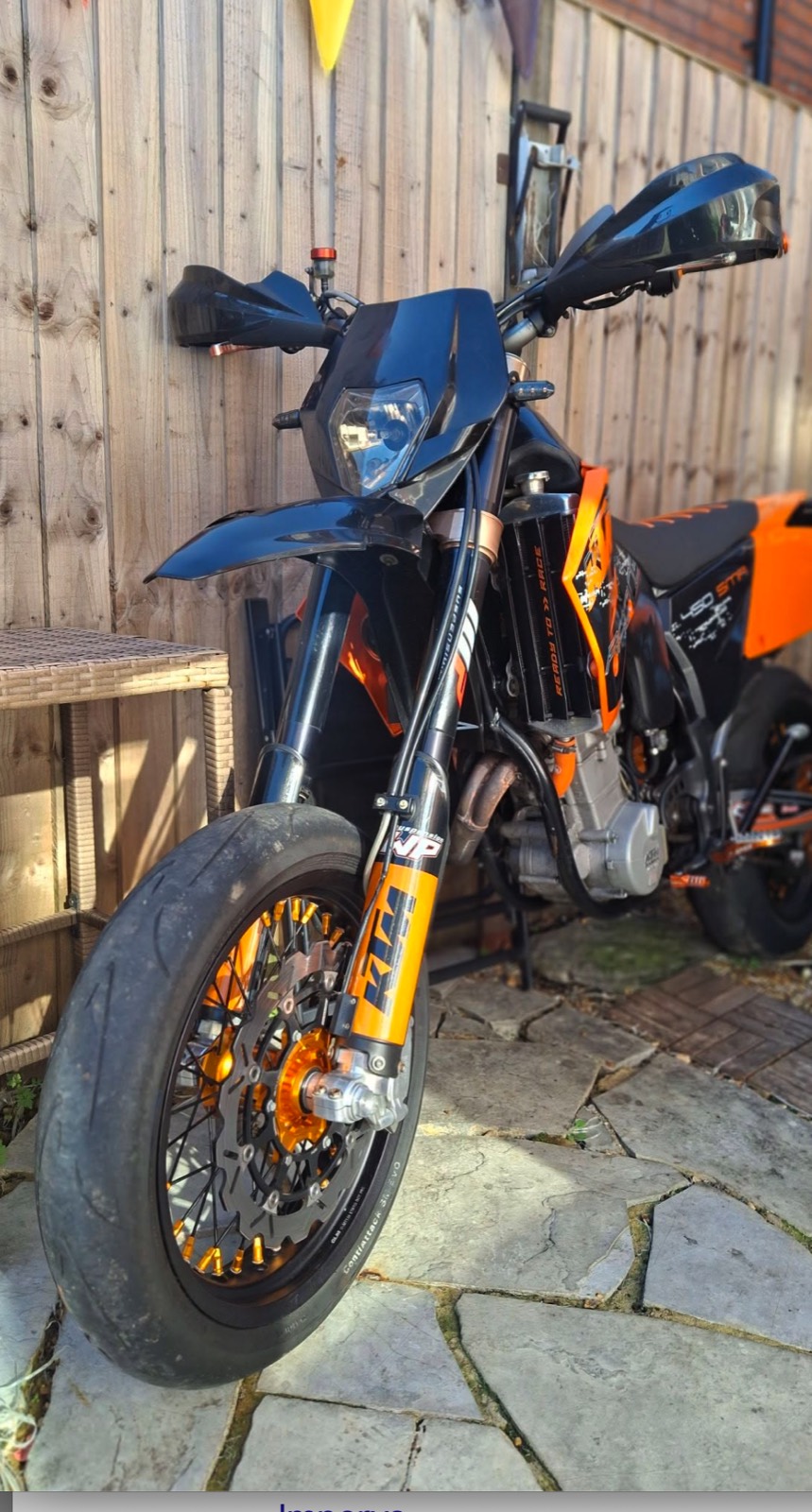 A black and orange KTM 450 SMR supermoto against a wooden fence