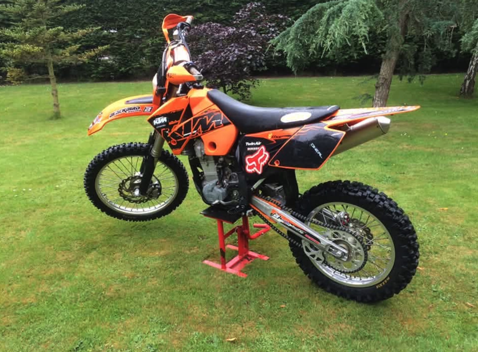 An orange and black KTM on a red stand in a garden