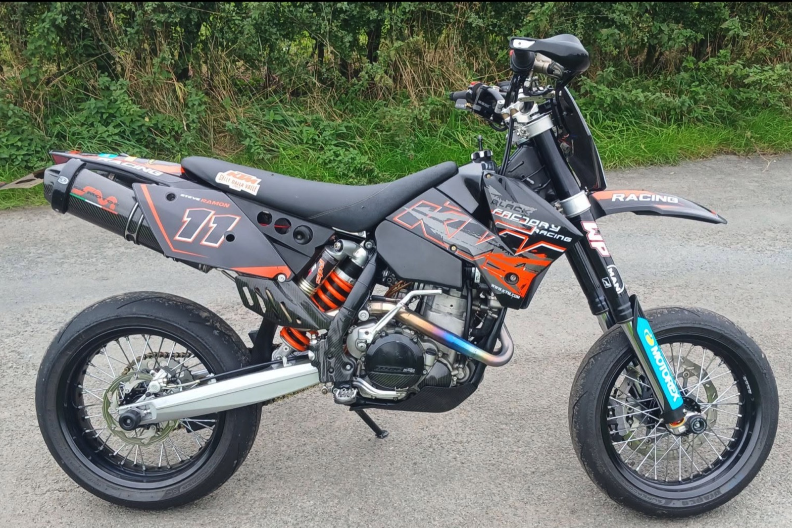 A black KTM supermoto with number 11 and orange graphics on a country lane