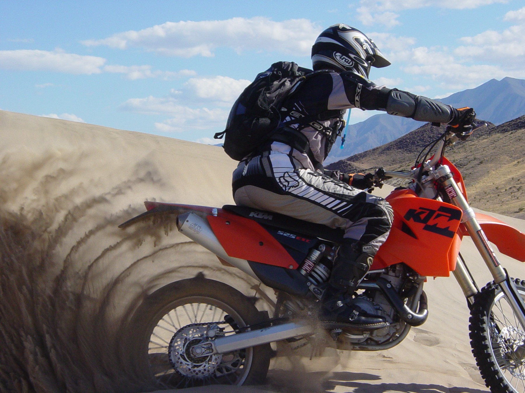 A rider on a 2004 KTM 525 EXC with a paddle tire throwing sand up a dune at Dumont Dunes, California