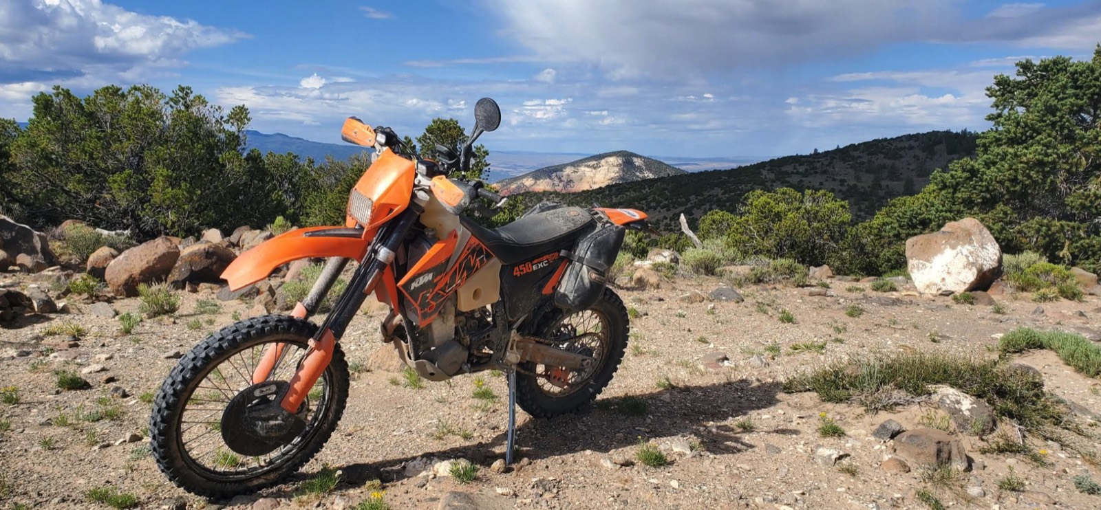 A KTM 450 EXC with handguards and a tail bag parked on a rocky ridge above a valley